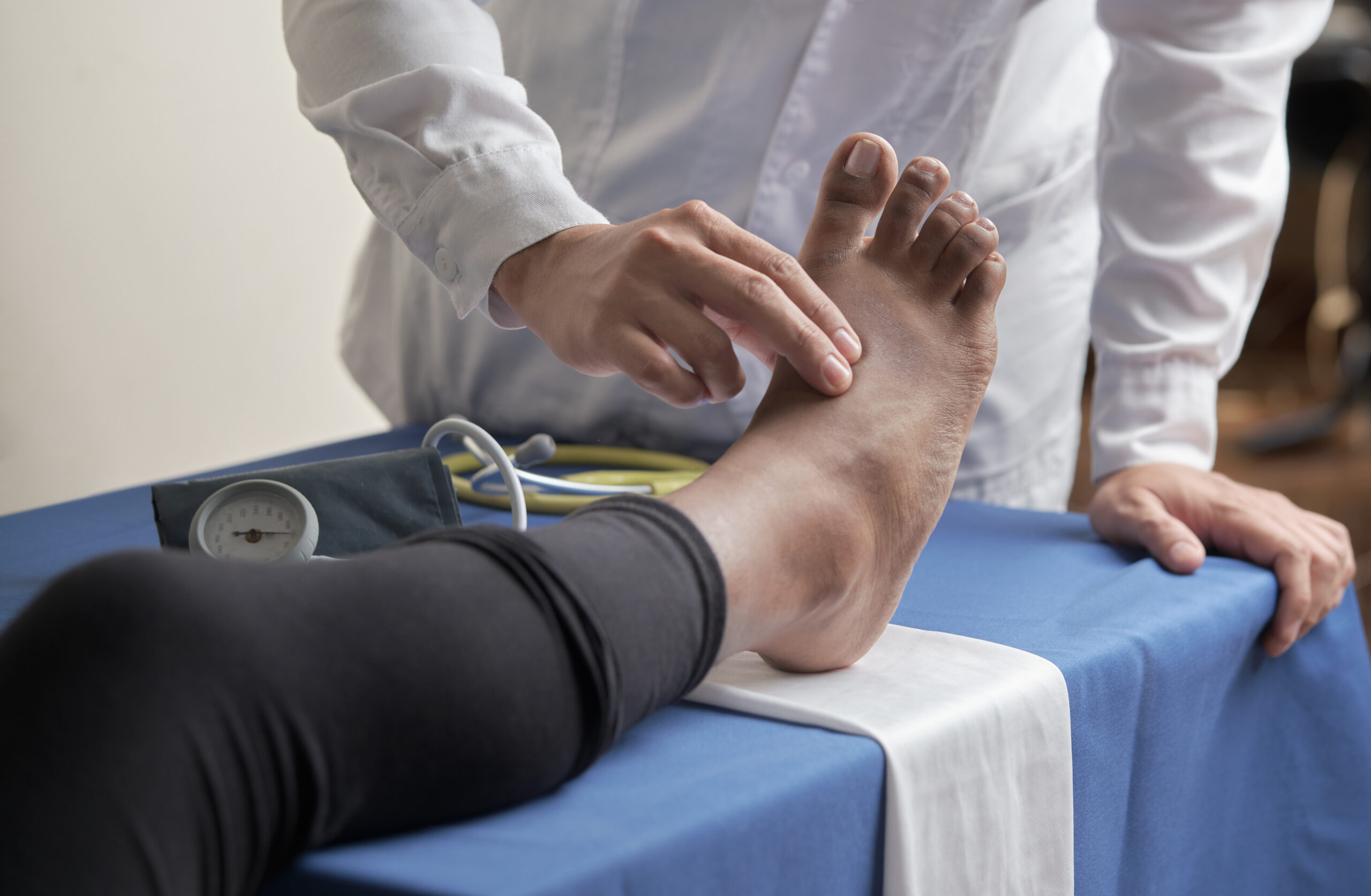 Doctor palpates patients pedial pulse for circulation assessment in medical office setting.