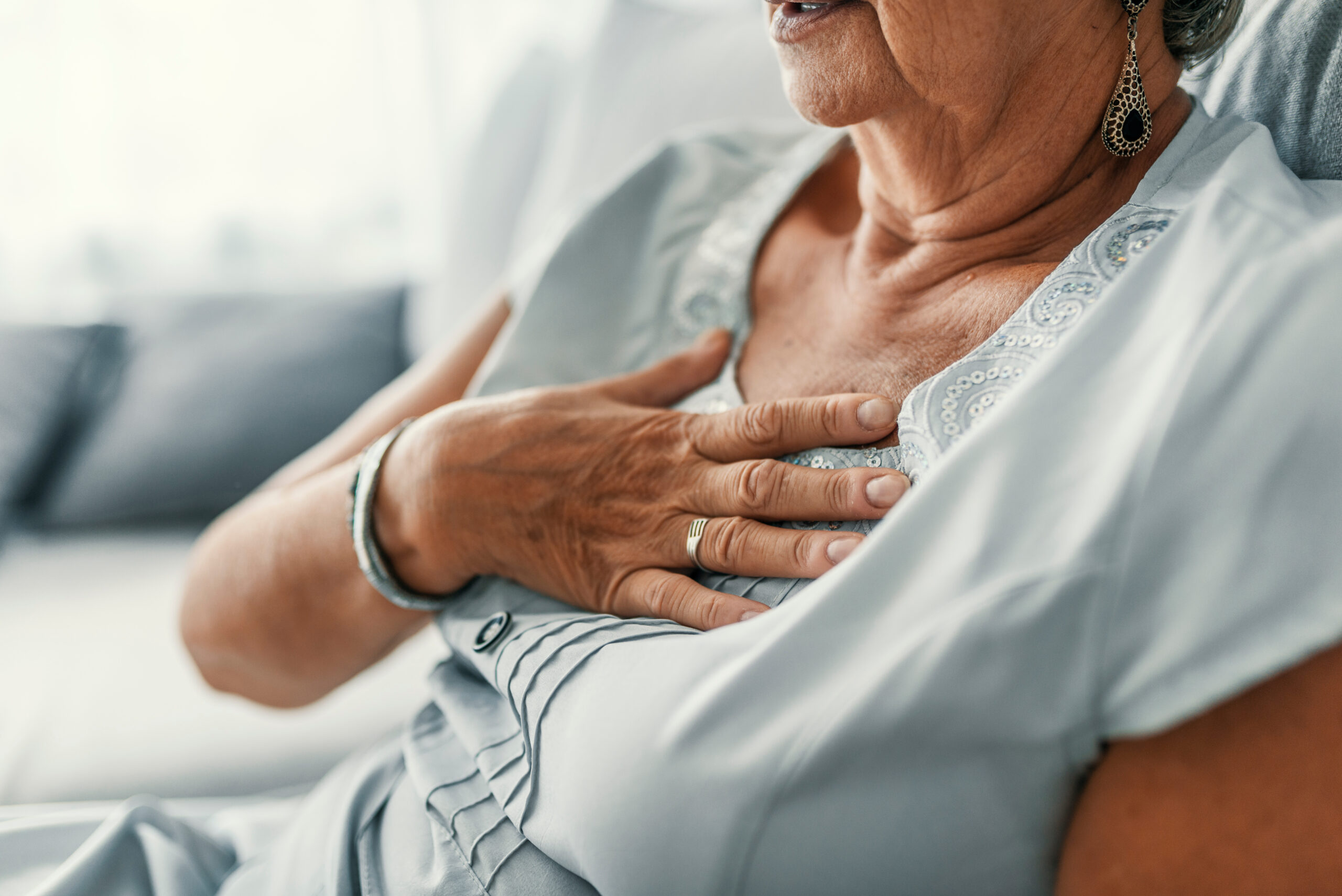 Senior woman with chest pain at home, highlighting potential heart or digestive issues.
